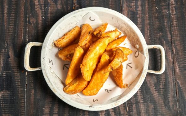 Golden crispy potato wedges served in a rustic white bowl on wood.