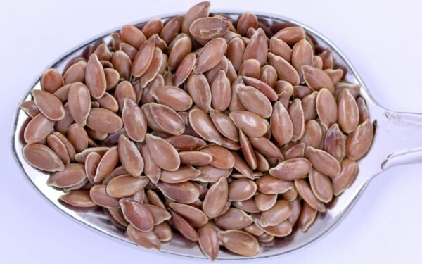 High-resolution close-up of flaxseeds on a metal spoon, showcasing detail and texture.