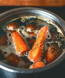 A close-up of carrots and potatoes boiling in a metal pot on a stove.