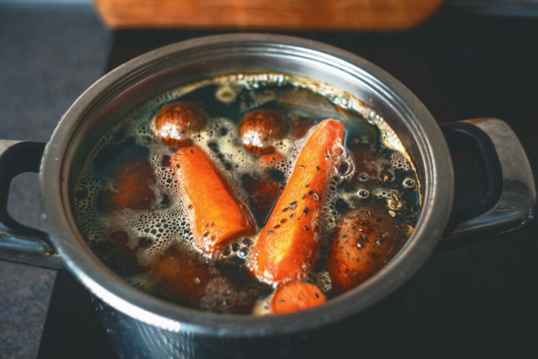 A close-up of carrots and potatoes boiling in a metal pot on a stove.