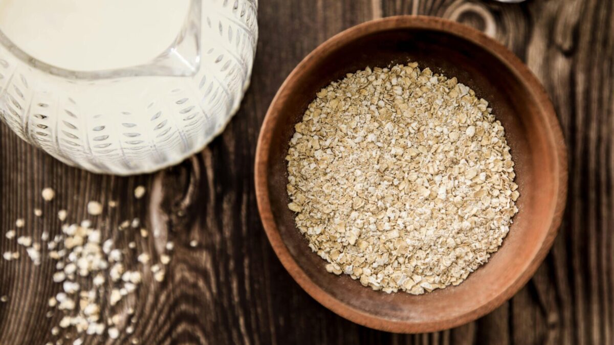 Wooden bowl of oats with milk jug on rustic table. Ideal for health-focused breakfast imagery.