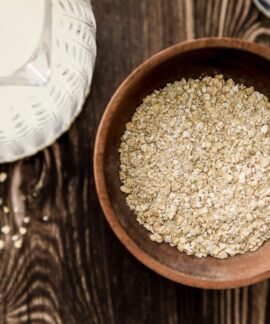 Wooden bowl of oats with milk jug on rustic table. Ideal for health-focused breakfast imagery.