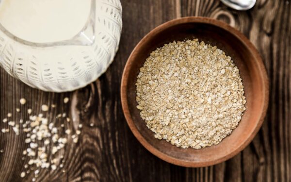 Wooden bowl of oats with milk jug on rustic table. Ideal for health-focused breakfast imagery.