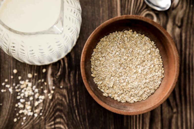 Wooden bowl of oats with milk jug on rustic table. Ideal for health-focused breakfast imagery.