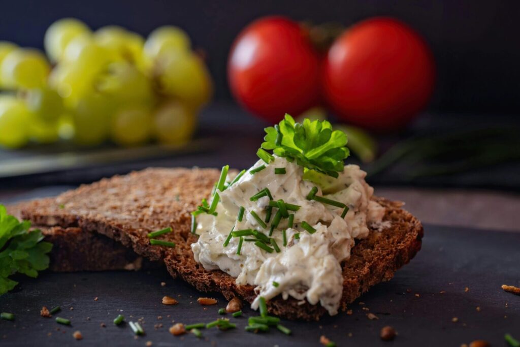 Appetizing wholegrain bread with cream cheese and herbs on a rustic dark background.