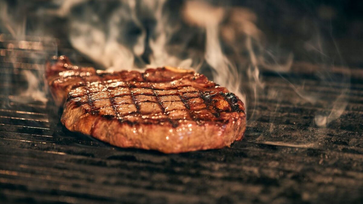 Close-up of a juicy grilled steak with smoke rising, sizzling on a barbecue grill.
