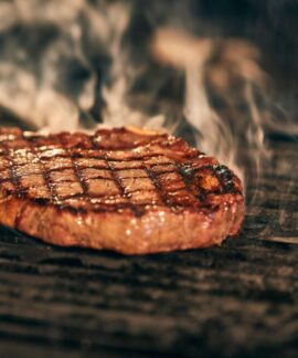 Close-up of a juicy grilled steak with smoke rising, sizzling on a barbecue grill.