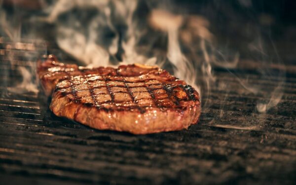 Close-up of a juicy grilled steak with smoke rising, sizzling on a barbecue grill.