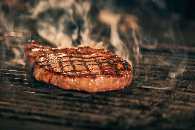 Close-up of a juicy grilled steak with smoke rising, sizzling on a barbecue grill.