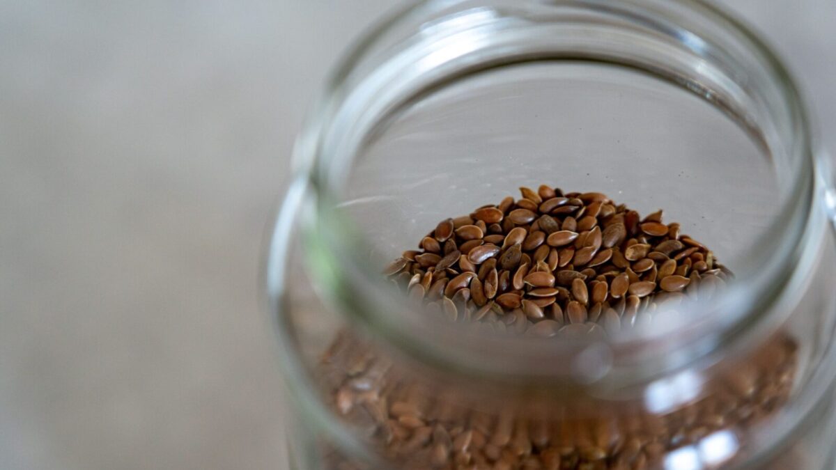 A clear glass jar filled with brown flax seeds, perfect for healthy cooking and baking.