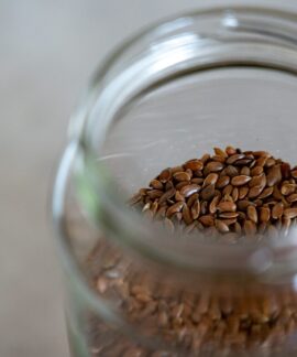 A clear glass jar filled with brown flax seeds, perfect for healthy cooking and baking.