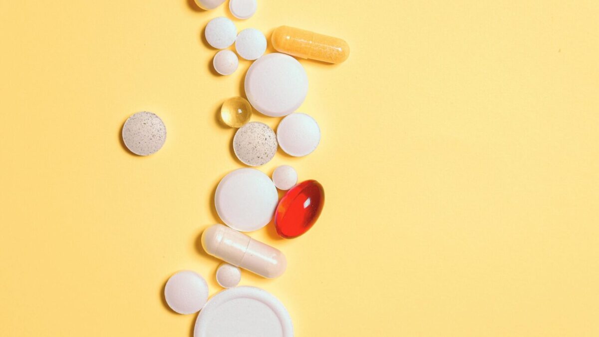 A collection of assorted pills and capsules on a vibrant yellow surface.