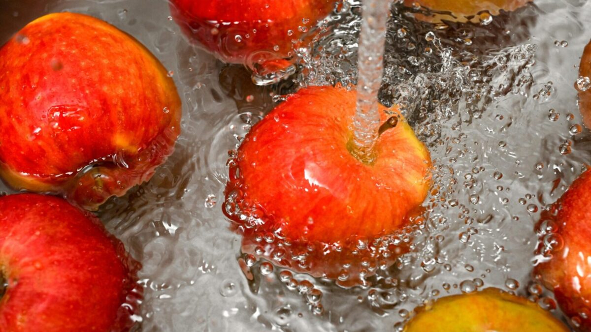 Vibrant red apples under a water stream, promoting cleanliness and freshness.