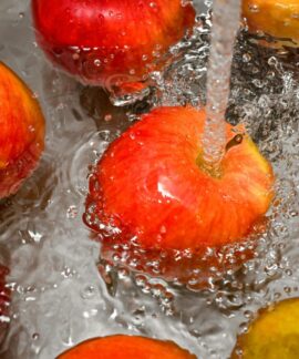 Vibrant red apples under a water stream, promoting cleanliness and freshness.
