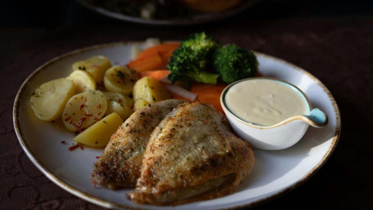 Delicious grilled chicken served with vegetables and creamy sauce on a plate.