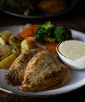 Delicious grilled chicken served with vegetables and creamy sauce on a plate.