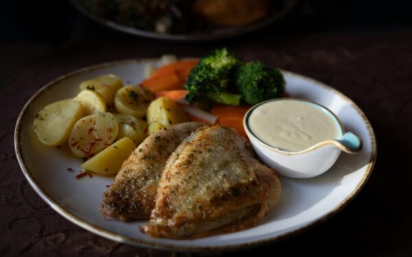 Delicious grilled chicken served with vegetables and creamy sauce on a plate.