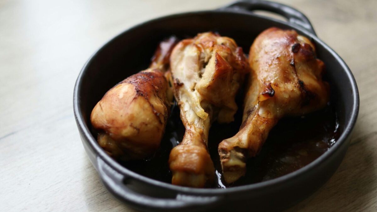 Tasty roasted chicken drumsticks served in a black cast iron pan on a wooden table.