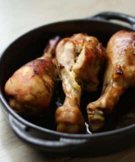 Tasty roasted chicken drumsticks served in a black cast iron pan on a wooden table.