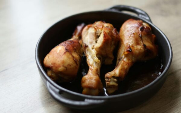 Tasty roasted chicken drumsticks served in a black cast iron pan on a wooden table.