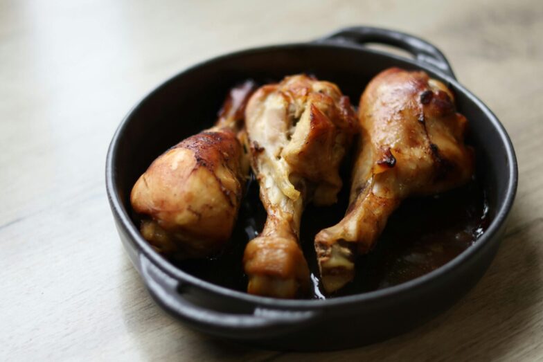 Tasty roasted chicken drumsticks served in a black cast iron pan on a wooden table.