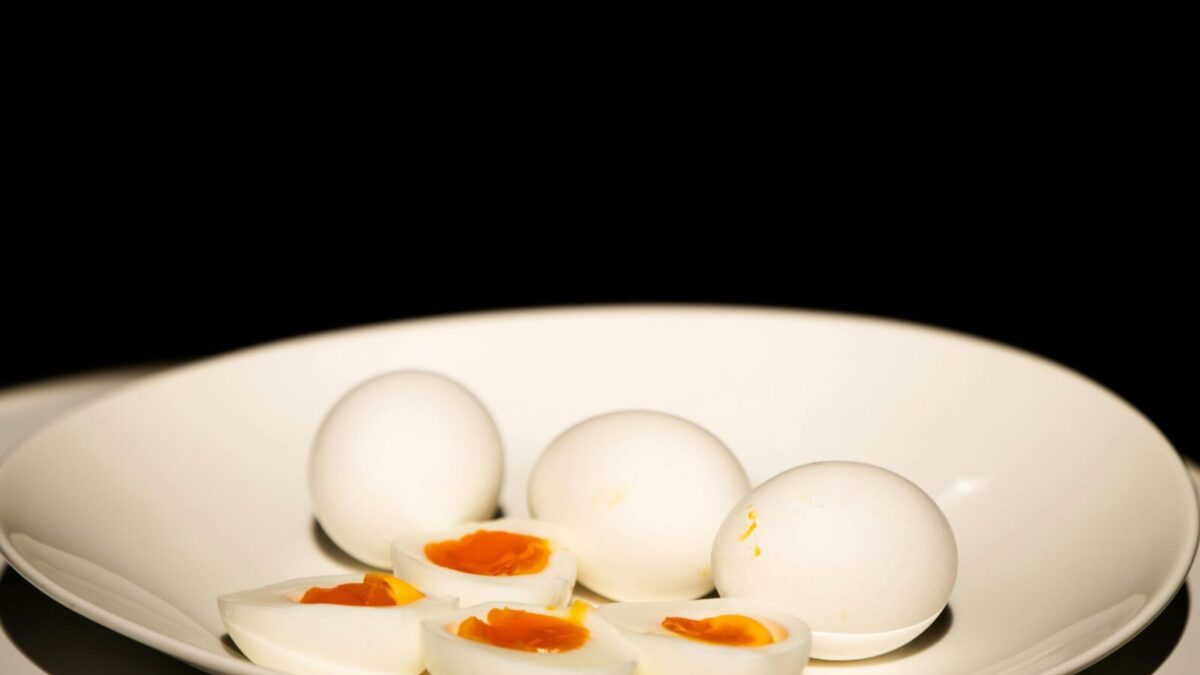 A white plate of hard-boiled eggs, some sliced, against a dark background.