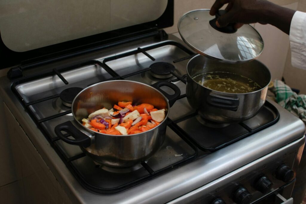A kitchen scene featuring fresh vegetables being cooked in pots on a gas stove.