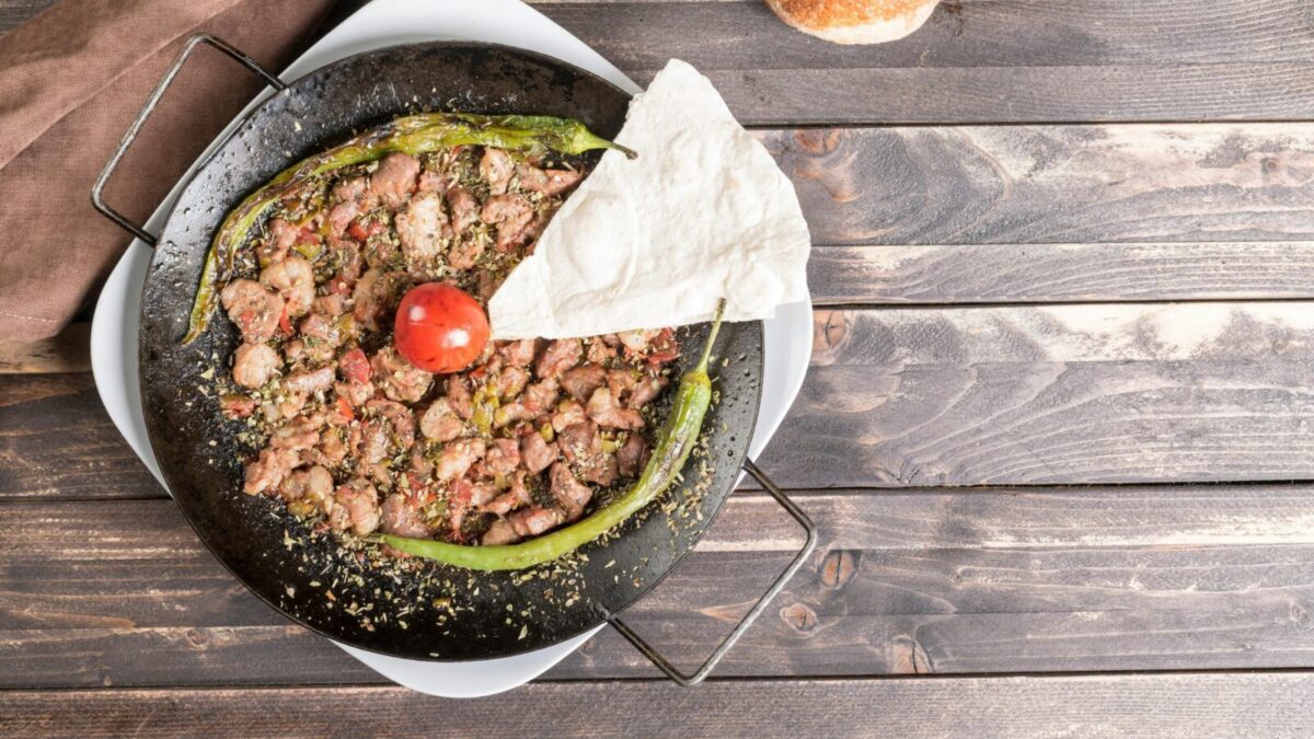 Delicious Turkish sautéed meat dish with peppers and tomato on a rustic wooden table.