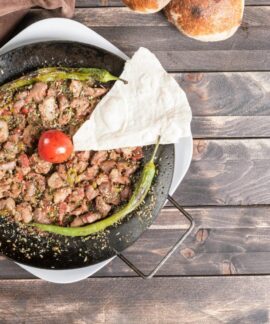 Delicious Turkish sautéed meat dish with peppers and tomato on a rustic wooden table.