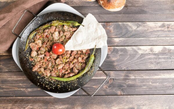 Delicious Turkish sautéed meat dish with peppers and tomato on a rustic wooden table.