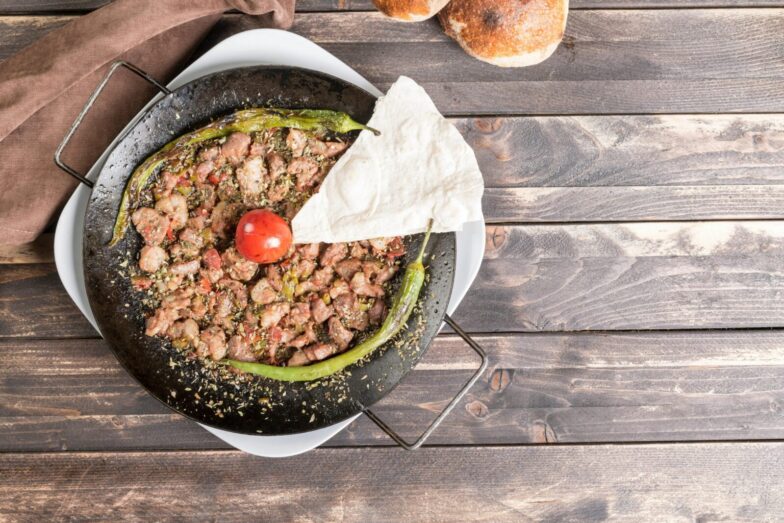Delicious Turkish sautéed meat dish with peppers and tomato on a rustic wooden table.