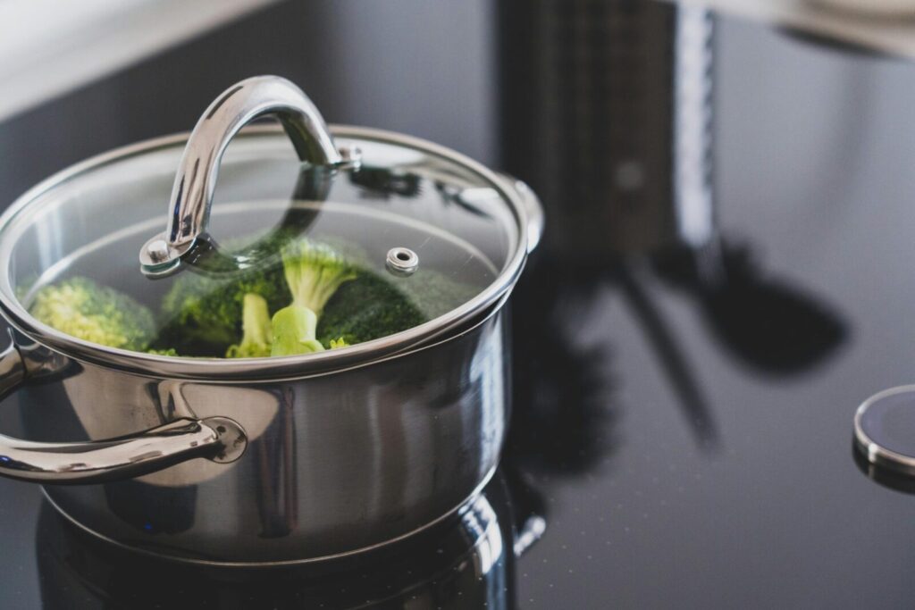 Close-up of broccoli steaming in a stainless steel pot on a modern stovetop indoors.