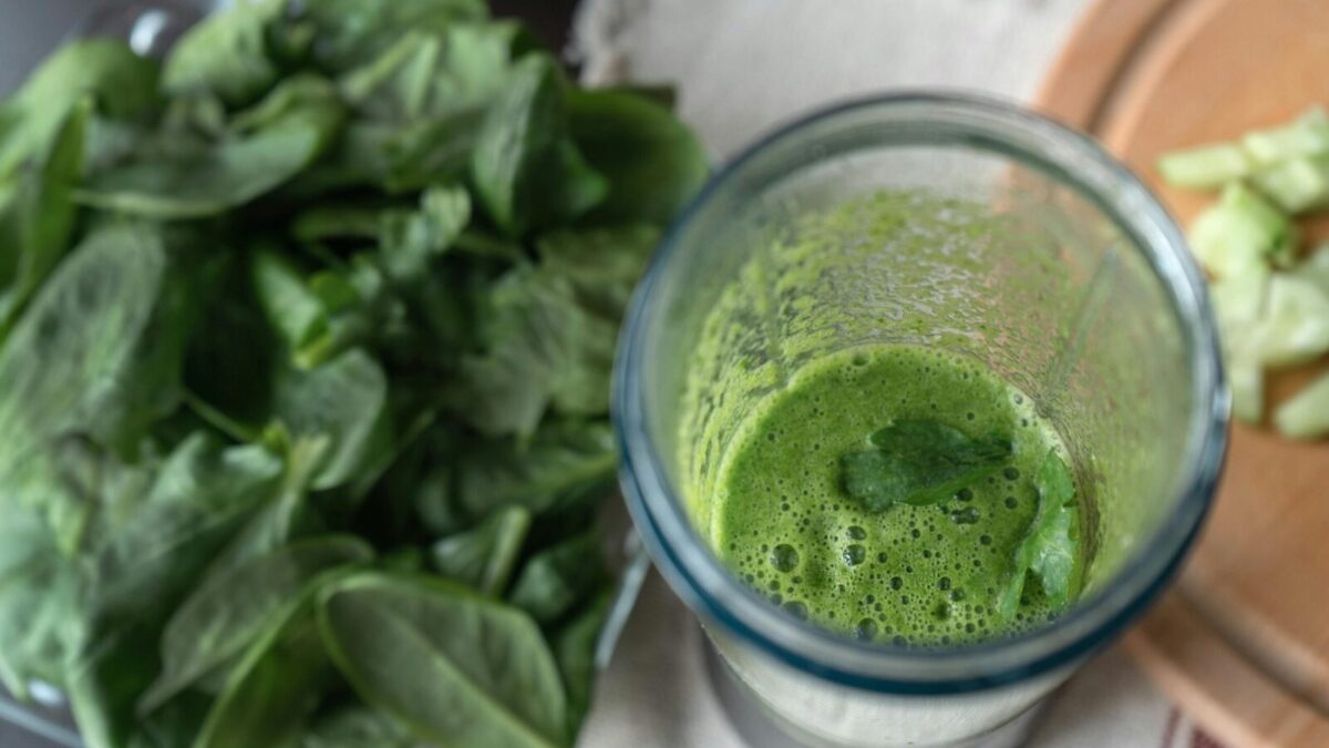 A refreshing green smoothie made with fresh spinach and cucumber on a wooden board.