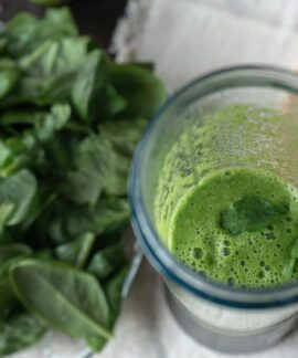 A refreshing green smoothie made with fresh spinach and cucumber on a wooden board.