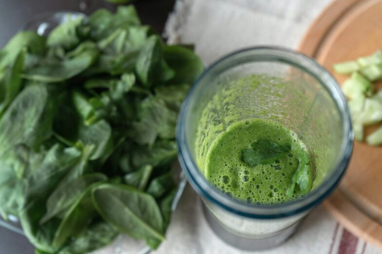 A refreshing green smoothie made with fresh spinach and cucumber on a wooden board.