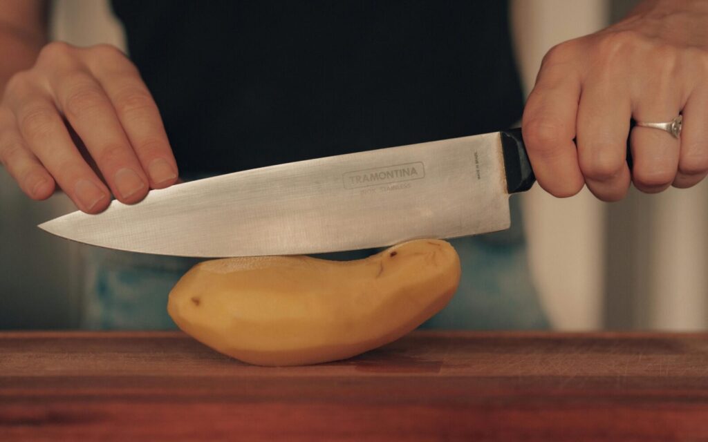 Close-up of hands slicing a potato with a kitchen knife, emphasizing cooking preparation.
