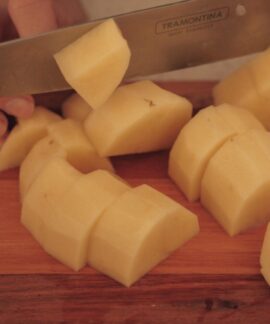 A person cuts potatoes on a wooden board with a kitchen knife.