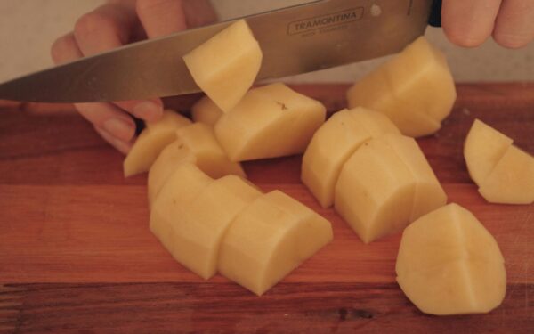 A person cuts potatoes on a wooden board with a kitchen knife.