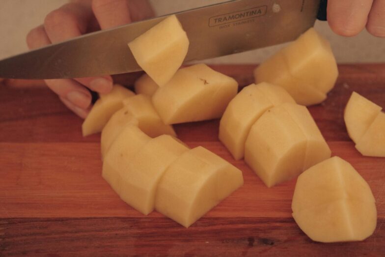 A person cuts potatoes on a wooden board with a kitchen knife.