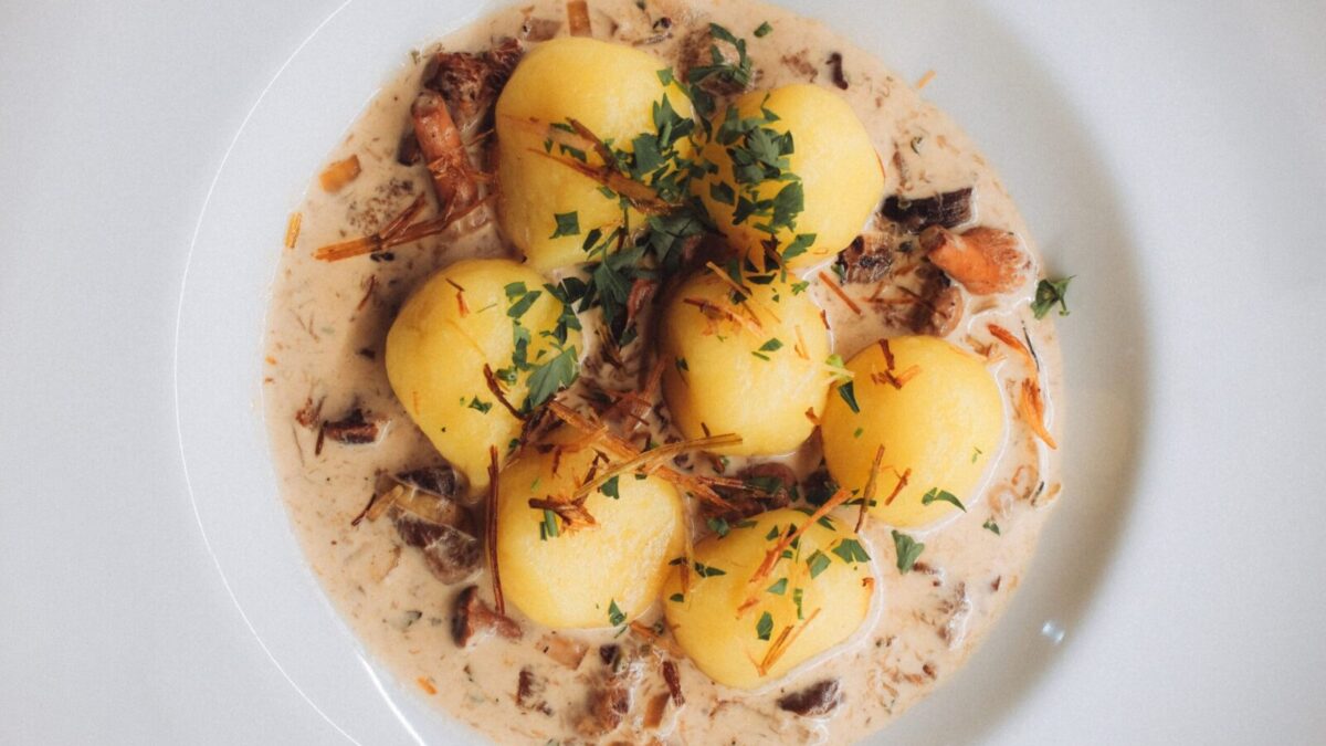 Close-up of traditional Polish dumplings served with a savory cream and mushroom sauce, garnished with fresh parsley.