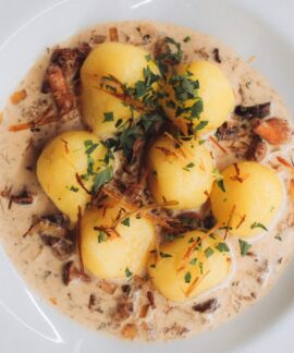 Close-up of traditional Polish dumplings served with a savory cream and mushroom sauce, garnished with fresh parsley.