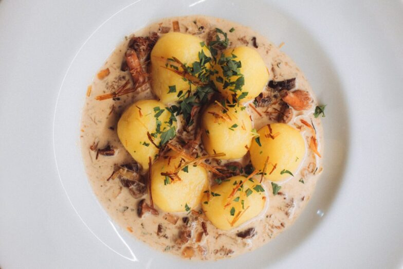 Close-up of traditional Polish dumplings served with a savory cream and mushroom sauce, garnished with fresh parsley.
