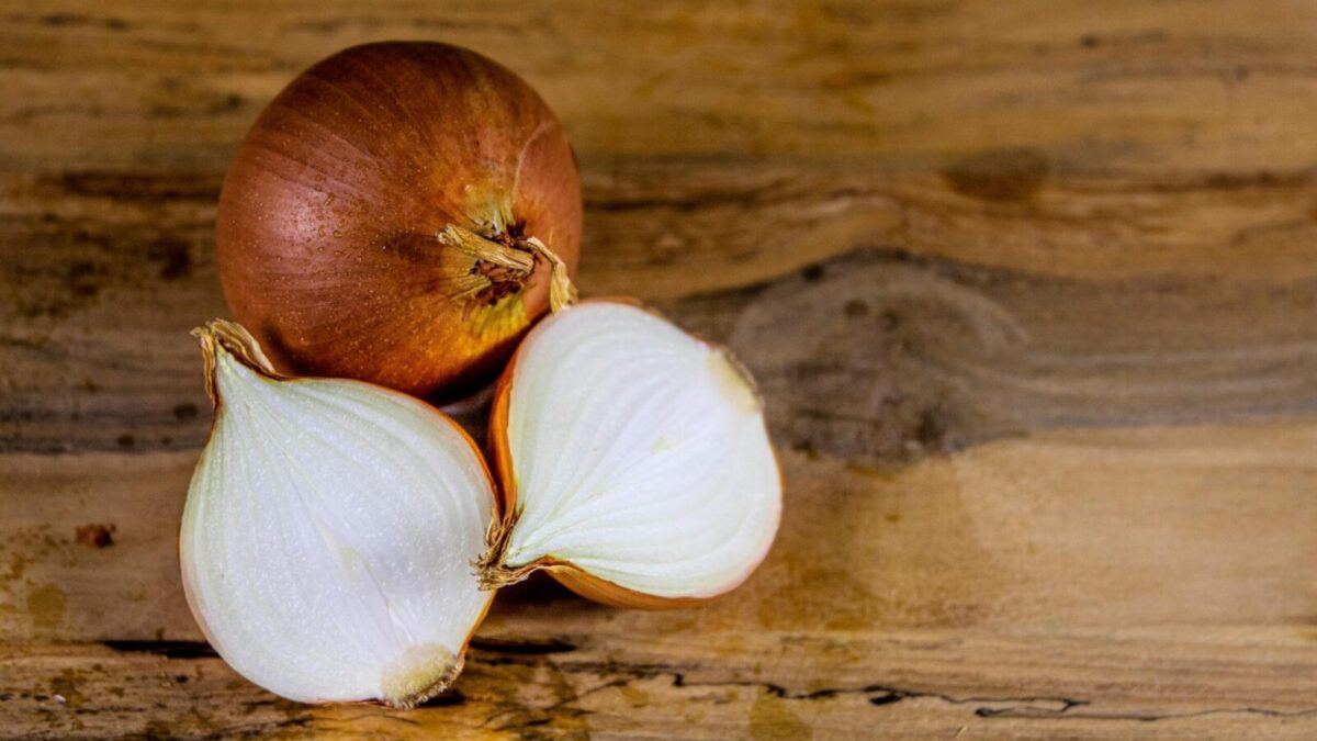 Detailed view of a whole and sliced onion on a textured wooden surface.