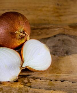 Detailed view of a whole and sliced onion on a textured wooden surface.