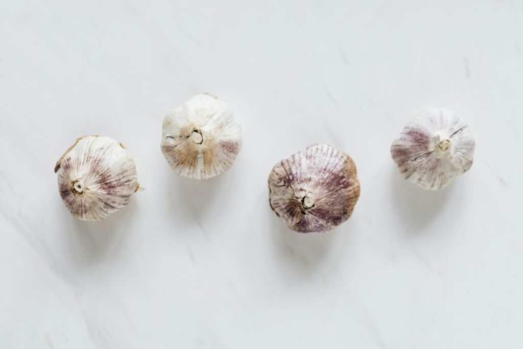 Top view of raw whole unpeeled aromatic garlic placed next to each other on white marble surface before cooking process