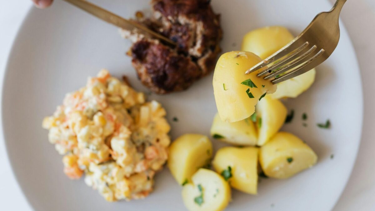 Top view of crop unrecognizable person eating fried juicy beef cutlet near delicious Russian salad with meat and boiled potatoes topped with parsley