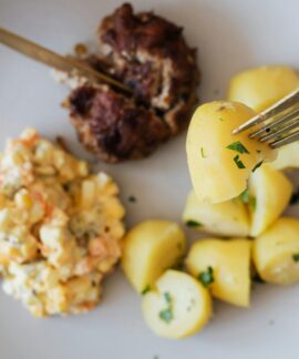 Top view of crop unrecognizable person eating fried juicy beef cutlet near delicious Russian salad with meat and boiled potatoes topped with parsley