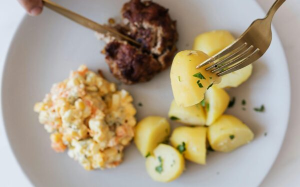 Top view of crop unrecognizable person eating fried juicy beef cutlet near delicious Russian salad with meat and boiled potatoes topped with parsley