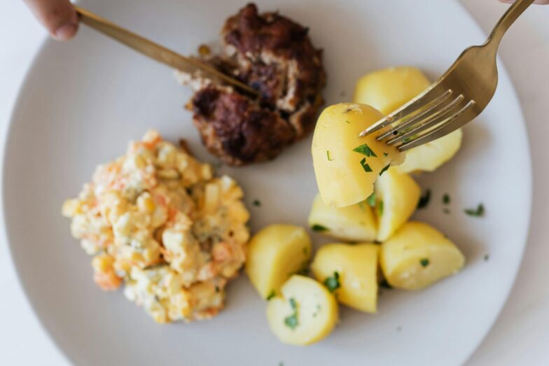 Top view of crop unrecognizable person eating fried juicy beef cutlet near delicious Russian salad with meat and boiled potatoes topped with parsley