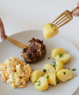 From above of crop anonymous person with cutleries eating delicious fried cutlet and hot boiled potatoes with parsley garnished with nutritious Russian salad